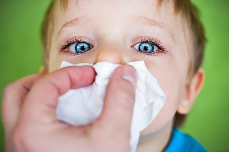 Child getting a tissue on his nose by an adult