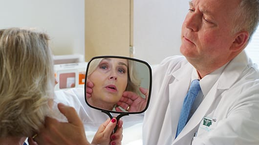 Physican lifting woman's face, while she holds the mirror to see